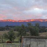 Sunrise in the Capertee Valley, the early morning rays reflecting of the sandstone cliffs of Genowlan Mountain. Farm in the foreground with a cement water tank and some cattle feeding.Low undulating green hills in the foreground.
