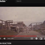 A screenshot of the movie “The Chain Reaction”, which is on YouTube. It shows men in Hazmat suits in the foreground wielding hoses and in the background is the structure of the ruins of Glen Davis Shale Works.