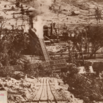 Historical picture of the Torbane Oil shale works, Capertee Valley NSW.It shows a picture of Rail line in the foreground, with the shale works retort in the middle and houses in the background all set in the bushland around that area.